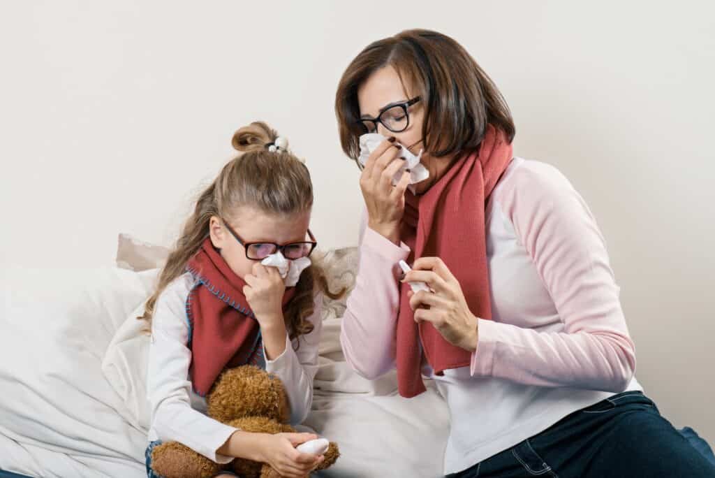 Sick mother and child sneezing in handkerchief, holding nasal spray, cold season