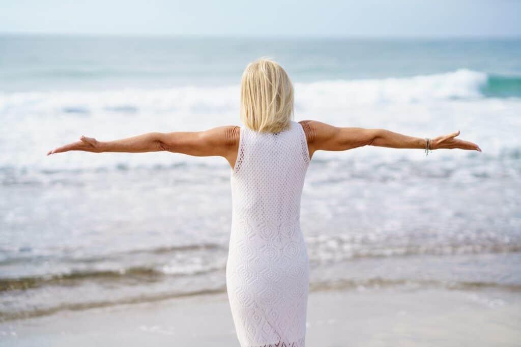 Anonymous mature woman with outstretched arms on seashore