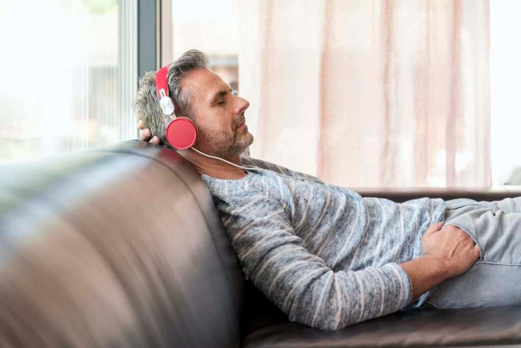 Relaxed mature man lying on couch at home wearing headphones