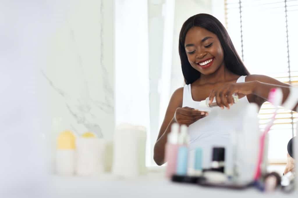 Skin Cleansing. Black Woman Pouring Micellar Water On Cotton Pad In Bathroom