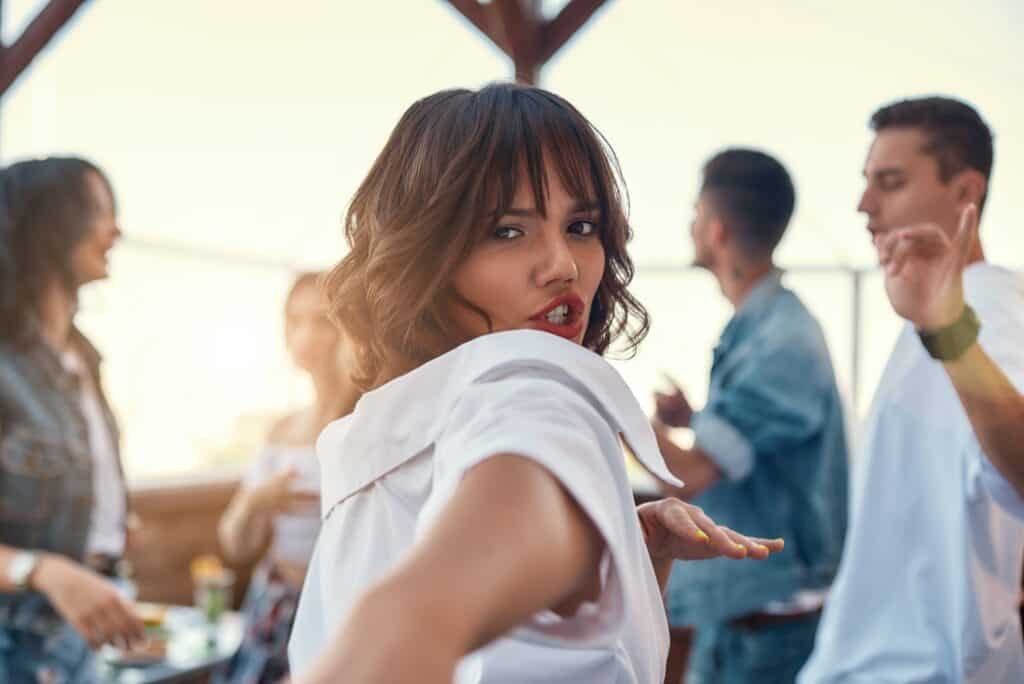 Full of energy. Pretty and young woman in white shirt is dancing and looking at camera while