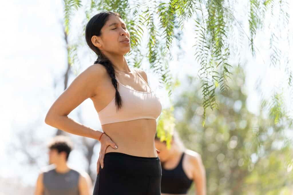 Hispanic young woman expresses back pain while doing sports