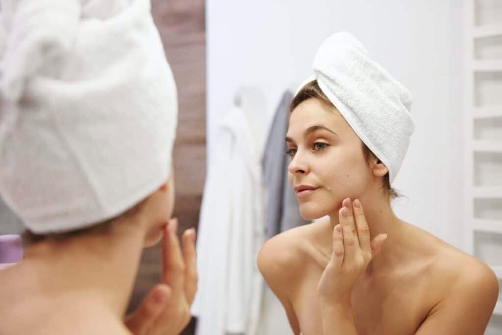 Mirror image of young woman examining her face in the bathroom