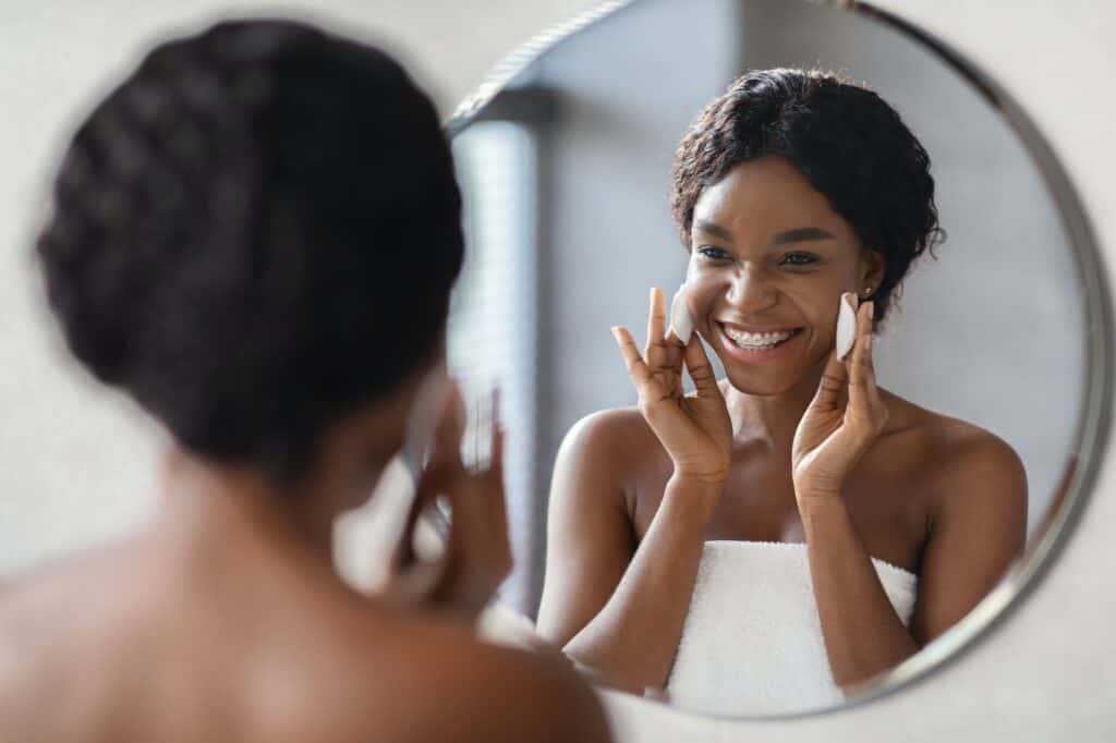 Positive african american woman removing makeup with cotton pads