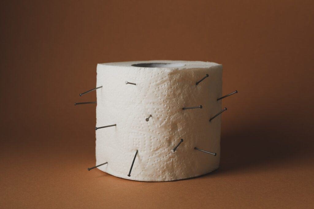 Toilet paper with nails on brown craft background. Hemorrhoids
