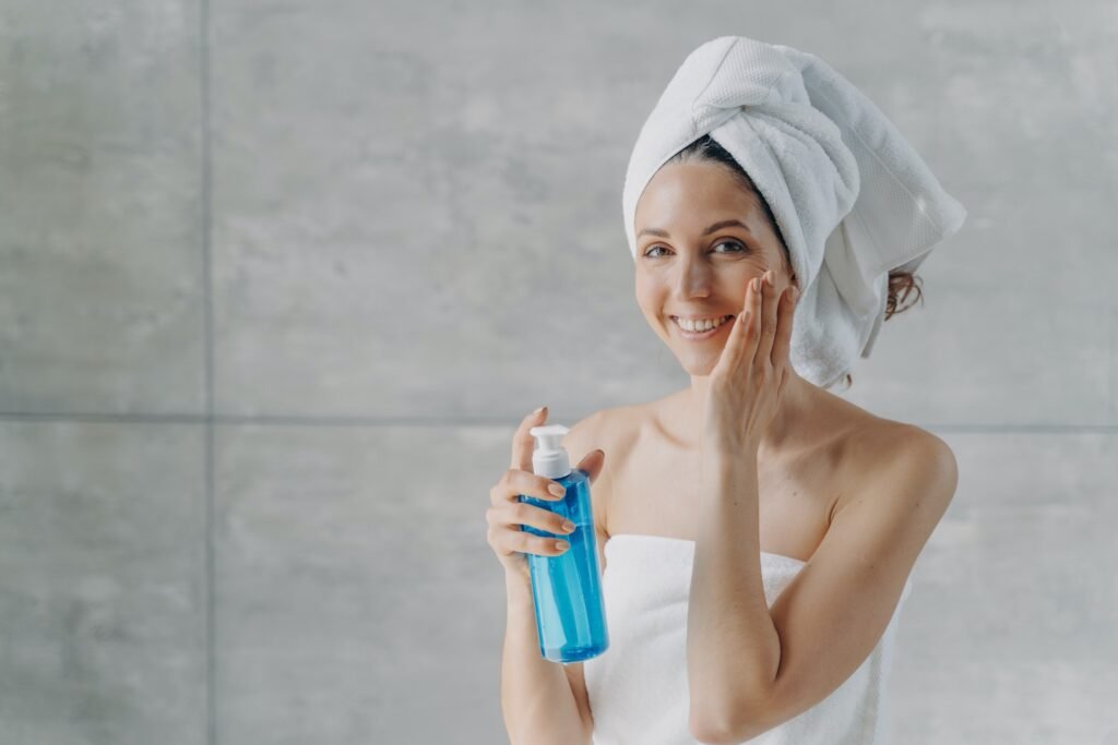 Face toner or micellar water. Gorgeous caucasian woman applying toner in flacon touching pure skin.