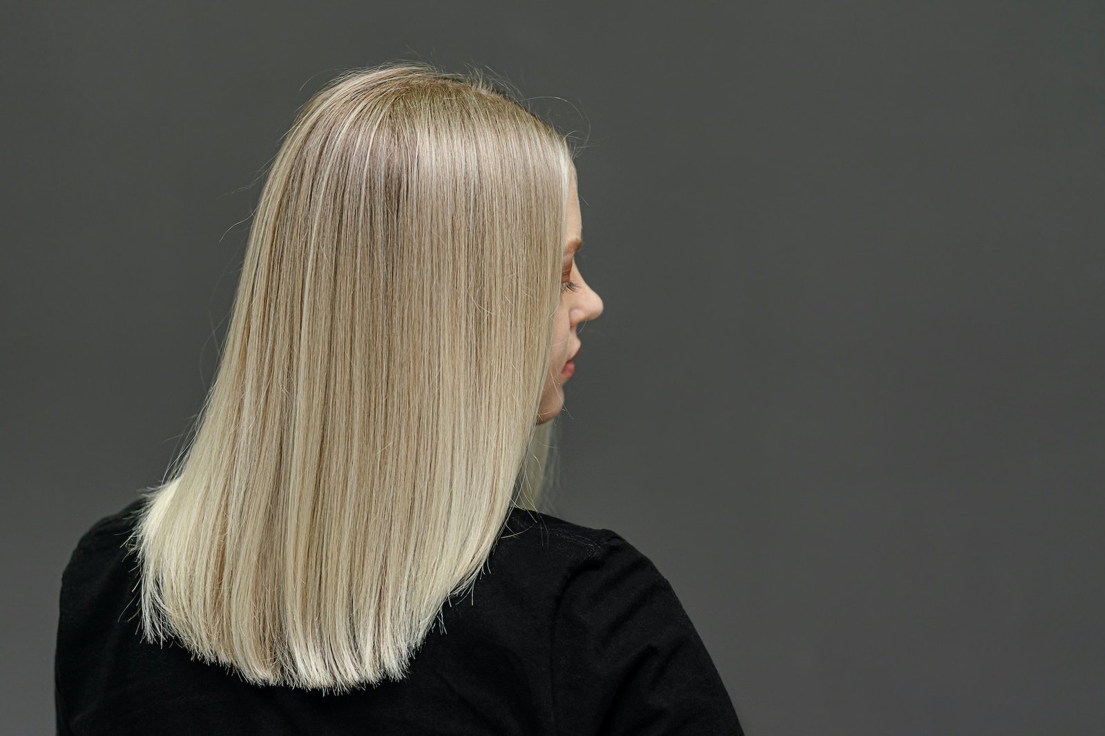 Blond modell med rett hår, se bakfra. Resultat av bleking av hår.