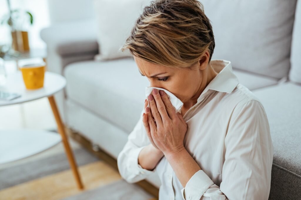 Businesswoman having a flue and blowing nose in a tissue at home.
