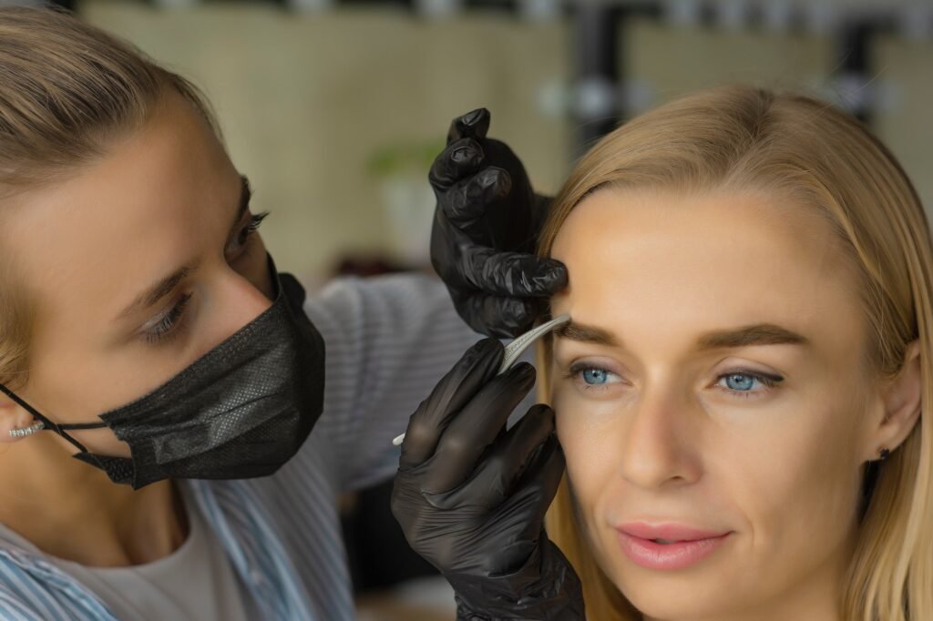 Close up side view of woman in salon doing eyebrow plucking with tweezers