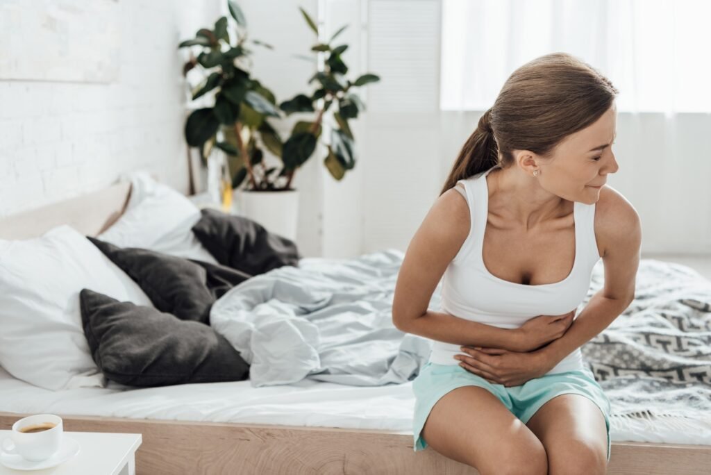 upset young woman sitting on bed and touching belly