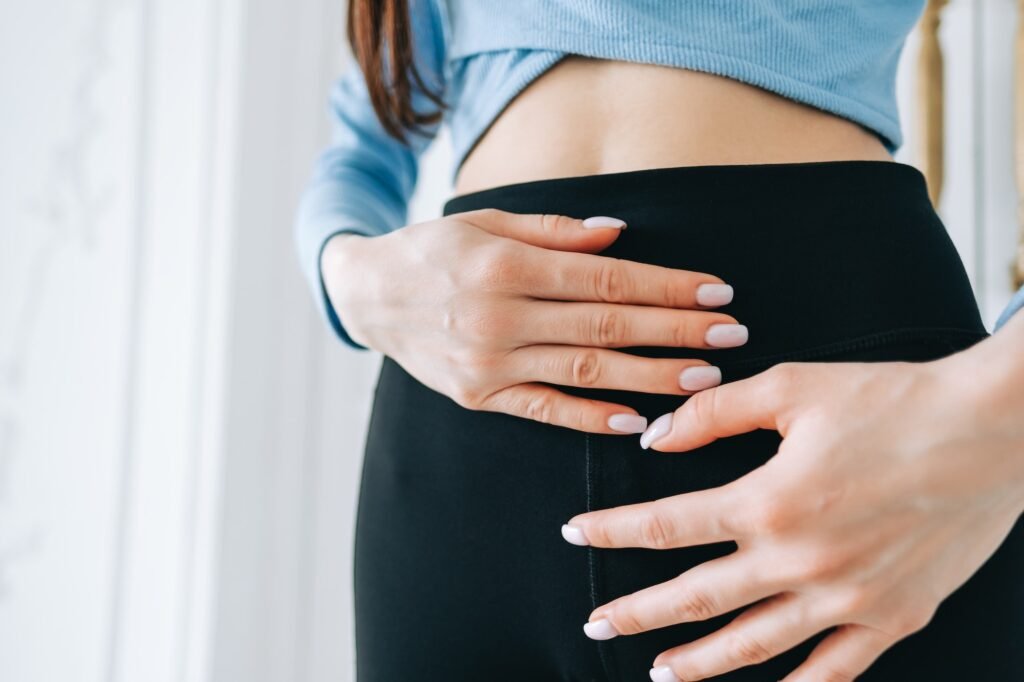 Young caucasian woman hands touching belly, close up.